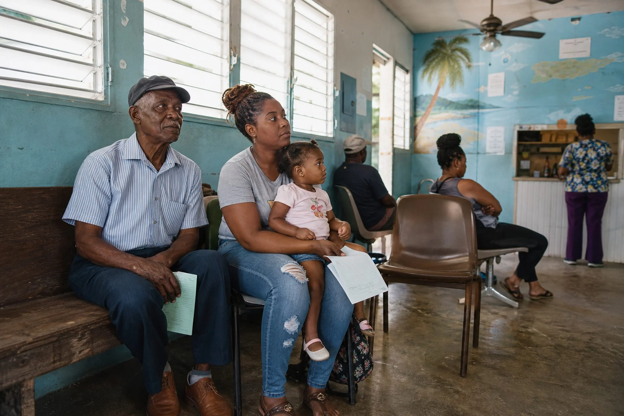 Patients wait on benches and chairs in a small island clinic waiting room, including an older man holding a form and a woman holding a toddler on her lap.